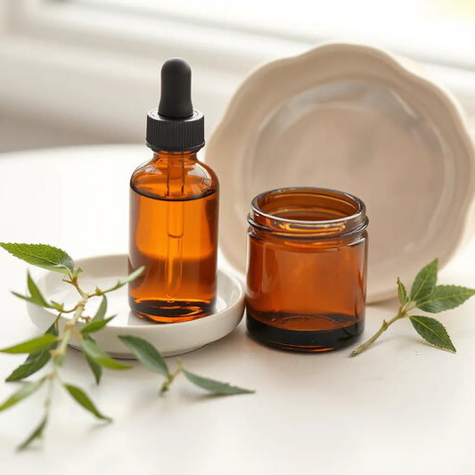 Herbal skincare dropper and balm jar with fresh green herb sprigs on a clean surface