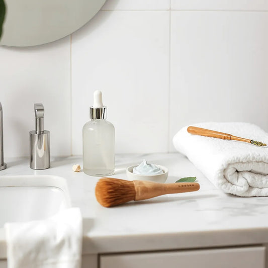 Skincare routine essentials on a clean vanity with dropper bottle, cream, and fresh botanical leaves