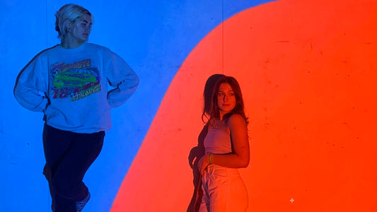 Two women against a wall illuminated by contrasting blue and orange light