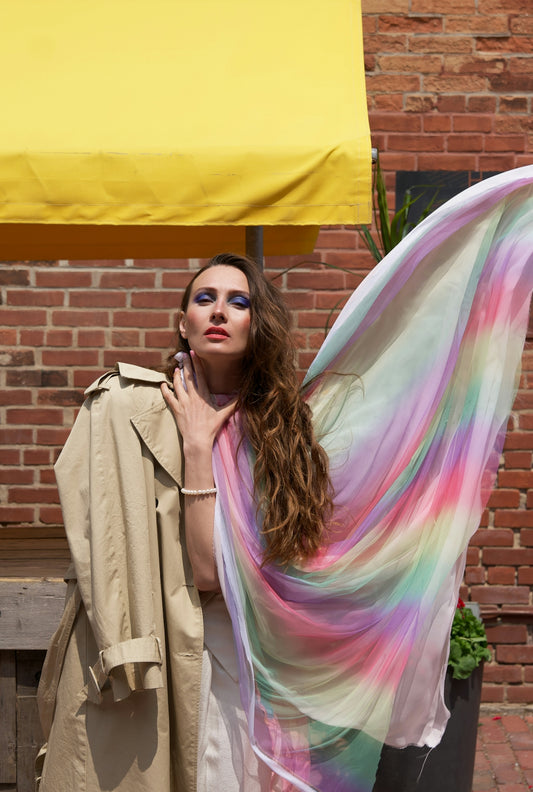 a woman is holding a colorful scarf in front of a brick wall