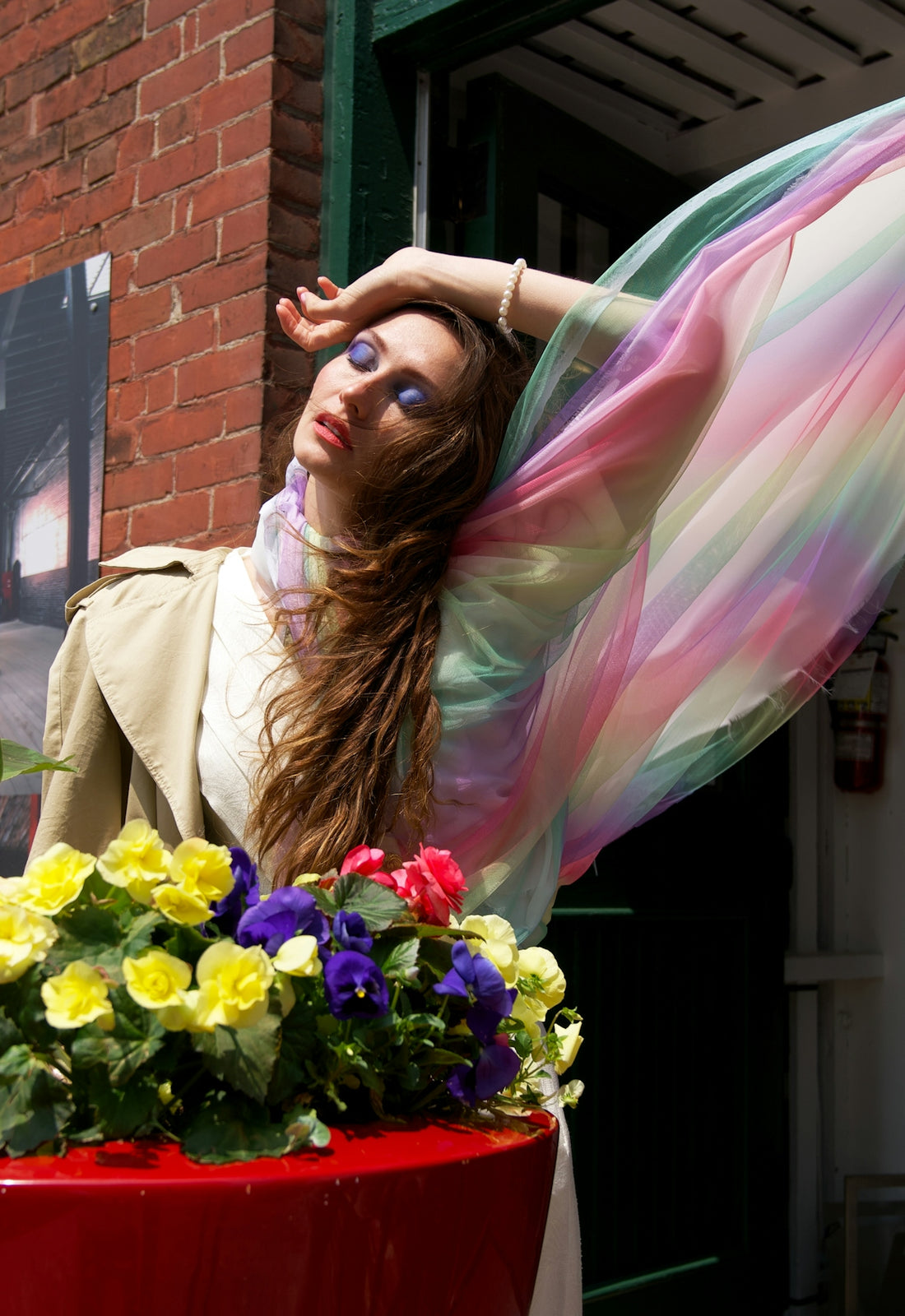 a woman with long hair and a colorful dress standing next to a flower pot